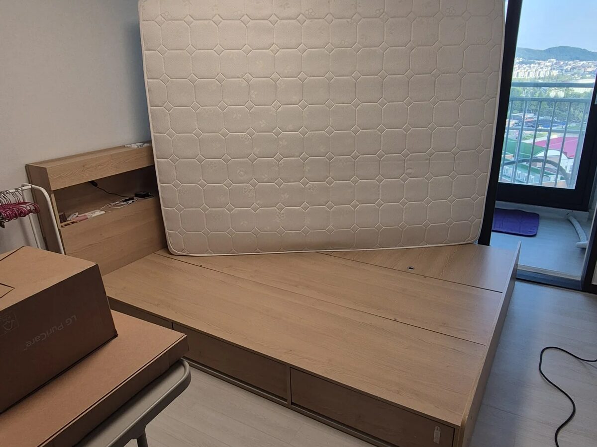 침대 헤드보드 뒷면과 프레임 이음새 틈새를 손전등으로 점검하는 장면